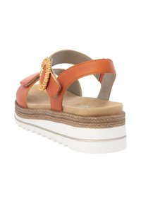 Sandale en cuir orange avec un cercle tissé décoratif, une sangle de cheville réglable et une semelle de plateforme stratifiée dotée d'une base marron texturée.