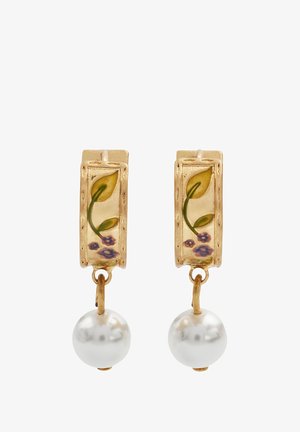 Boucles d'oreilles en or avec des sommets rectangulaires ornés de motifs floraux et des gouttes de perles blanches. Présente des feuilles vertes et des fleurs violettes sur une surface texturée.
