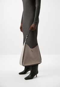Borsa hobo in pelle crema e taupe con motivo embossato. Caratterizzata da tracolla regolabile e forma strutturata. Visibili lunghi stivali neri con tacco.