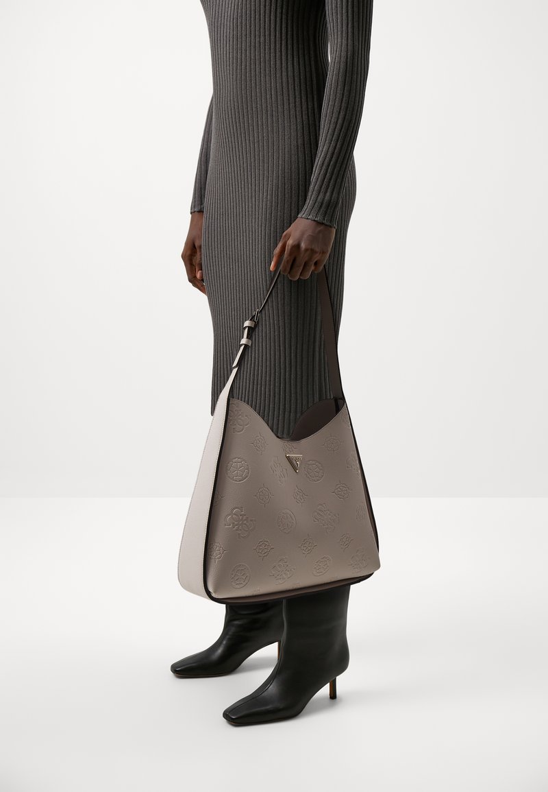 Sac à main hobo en cuir crème et taupe avec un motif en relief. Doté d'une bandoulière réglable et d'une forme structurée. Longs bottes noires à talons visibles.