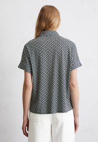 Kurzarmshirt mit geometrischem Schwarz-Weiß-Muster, Kragen und lockerer Passform, aus weichem Stoff gefertigt.