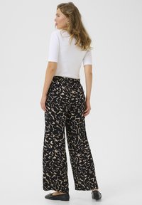 Pantalons larges noirs avec un motif abstrait beige, taille élastique, associés à un haut blanc ajusté et des chaussures noires plates.