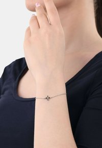Bracciale in argento con una delicata catena, caratterizzato da un design floreale con una pietra preziosa centrale rossa e due accenti bianchi su ciascun petalo.
