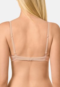 Sostén beige con tirantes ajustables, tela suave y una sutil banda elástica en la parte posterior. Diseño simple, textura suave y sin adornos visibles.