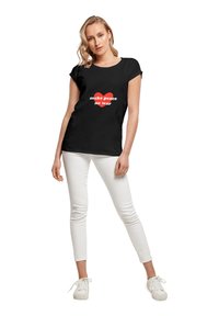 Sort T-shirt med rullekapærmer, der har et rødt hjertegrafik og teksten "make peace no war" i hvid. Sammen med hvide bukser og sneakers.