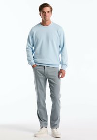 Lichtblauwe katoenen crewneck sweatshirt gecombineerd met lichtgrijze slim fit pantalon. Model draagt witte sneakers. Eenvoudig en modern ontwerp.