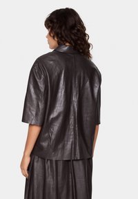 Leather jacket in dark brown, with short sleeves and a relaxed fit. Features a classic collar and smooth texture.