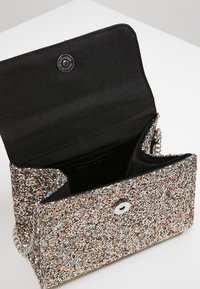 Błyszcząca srebrna torebka w wielokolorowe wzory o fakturowanej powierzchni, z magnetycznym zapięciem i czarnym materiałowym wnętrzem. Widoczny łańcuszkowy pasek na ramię.