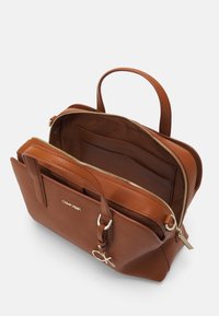 Ruskeasta nahasta valmistettu käsilaukku, jossa on jämäkkä muotoilu, kultasävyinen vetoketju, kaksi yläkahvaa ja brändilogolla varustettu. Sisätilassa on useita taskuja.