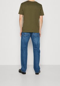 T-shirt di cotone verde oliva con maniche corte, abbinata a jeans in denim a gamba dritta di un blu chiaro. Scarpa nera testurizzata completa il look.