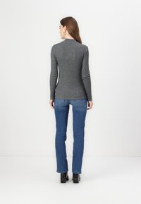 Grå langermet topp med høy hals, sammen med blå denim jeans. Jeansene har rett snitt og svak bleking på lårene.