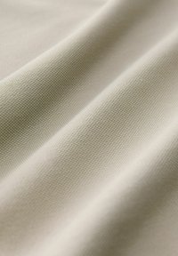 Tissu beige clair texturé présentant un motif de tissage subtil. Le matériau semble doux avec de légers plis et ondulations.