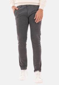 Pantaloni in cotone grigi con una vestibilità slim, dotati di tasche frontali e una cintura classica. Abbinati a sneaker bianche.