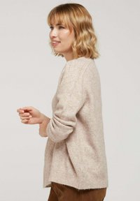 Pull en maille doux, rose clair, avec des manches longues, un col en V et des poignets côtelés. Coupe légèrement oversize avec des fentes sur les côtés à l'ourlet.