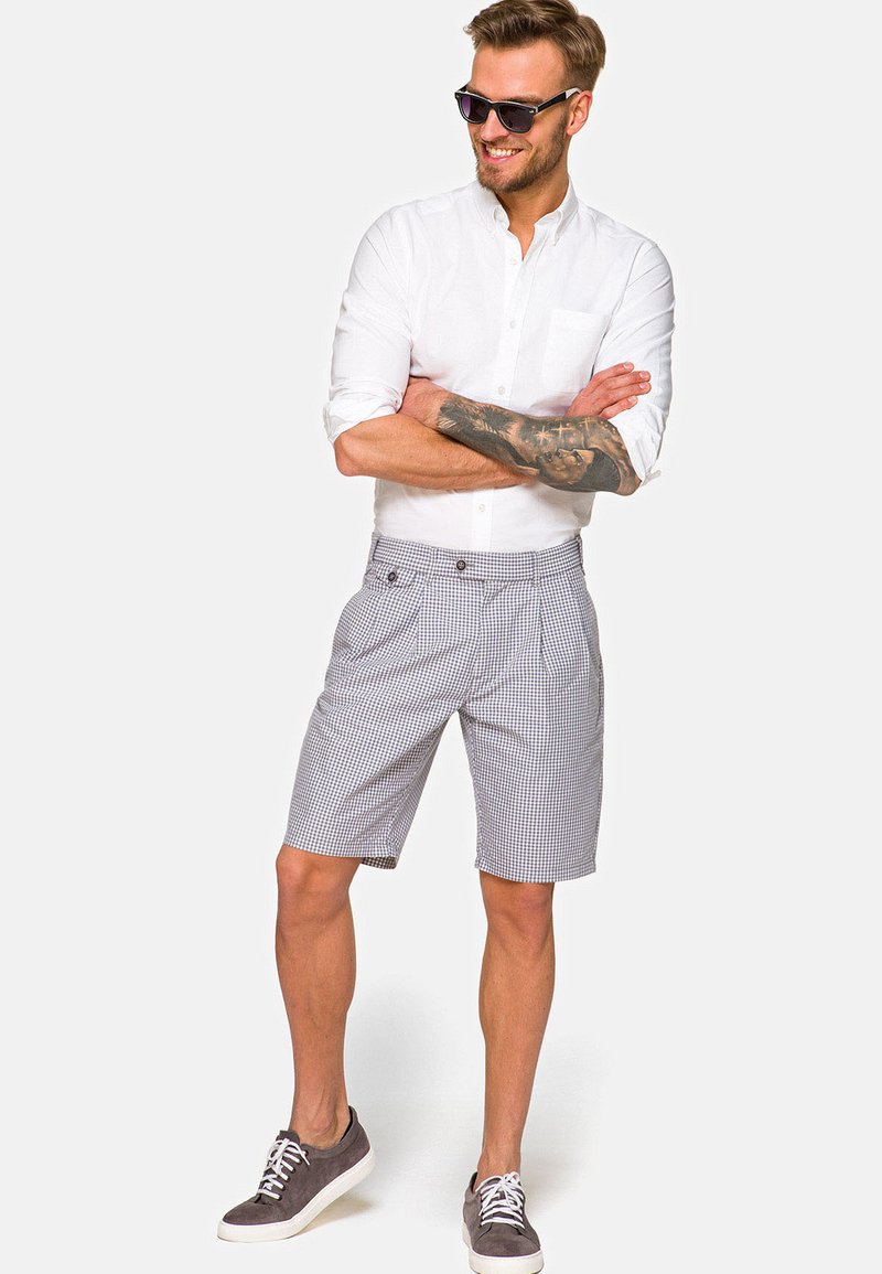 Męskie szorty w kratę w odcieniach szaro-białych, z płaskim przodem, bocznymi kieszeniami i wykończonymi mankietami. W połączeniu z białą koszulą z guzikiem i szarymi sneakerami.