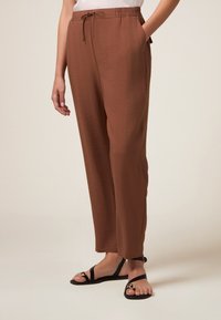 Pantalons beiges, légers et amples avec une taille élastique et un cordon de serrage. Poches latérales et texture lisse.