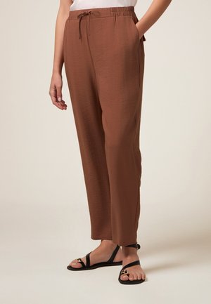 Pantaloni marroni, leggeri, a vestibilità larga con cintura elastica e cordoncino. Tasche laterali e una texture liscia.