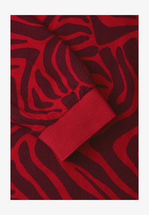 Rødt stof med mørkerøde abstrakte zebra-lignende striber og en ribbet manchet detalje på et ærme af et stykke tøj.