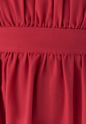 Červená látka s nařasenými sklady nad a pod hladkým horizontálním páskem, ukazující texturu a detaily šití.