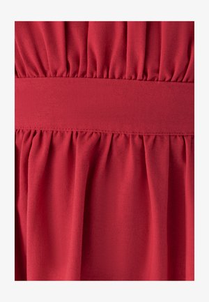 Roter Stoff mit gerafften Falten oben und unten an einem glatten horizontalen Bund, der Textur- und Stichdetails zeigt.