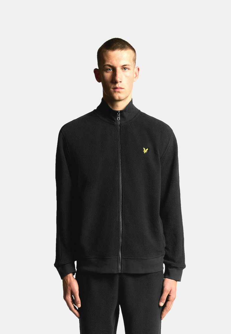 Schwarze Fleecejacke mit Reißverschluss und hohem Kragen. Verfügt über ein kleines gelbes Logo auf der linken Brustseite. Weiche Textur, eng anliegende Bündchen und Bund.