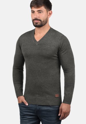 Suéter de cuello en V gris oscuro, hecho de un material suave, con mangas largas y un dobladillo acanalado. Pequeño acento de marca en el costado inferior.