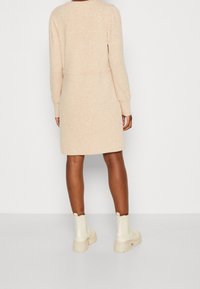 Robe en maille beige à manches longues, col rond, et motif texturé, portée avec des bottines blanches à semelle épaisse.