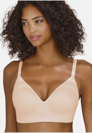 Woman with curly hair wearing a beige seamless bra, looking slightly to the side against a plain white background.