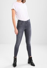 Grå smala jeans, kroppsnära silhuett, tygblandning av bomull, matchade med en enkel vit t-shirt och svarta ankelboots med detaljer. Slät textur.