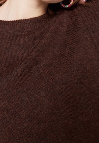 Hnědý pletený svetr s kulatým výstřihem, jemnou texturou a volným střihem, s jemnými barevnými a hloubkovými variacemi.