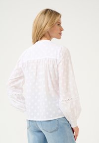 Witte blouse met opstaande mouwen, gestippelde textuur en kantaccenten op de manchetten. Detail met achteroverplatting en een ronde halsontwerp.