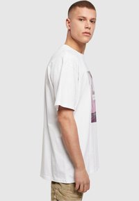 T-shirt blanc à manches courtes en coton avec un imprimé graphique à l'avant. Coupe droite et ajustement décontracté. Assorti à un short cargo beige clair.