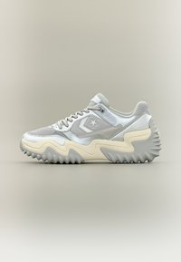 Λευκό και γκρι αθλητικό παπούτσι χαμηλού προφίλ με λογότυπο αστέρι, κυματιστή κρεμ σόλα και στιβαρή, αγκαθωτή εξωτερική σόλα σε ουδέτερο φόντο.