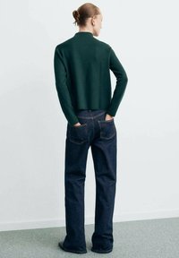 Maglione corto verde scuro abbinato a jeans dritti blu scuro. L'outfit presenta un design semplice con cuciture visibili e tasche.