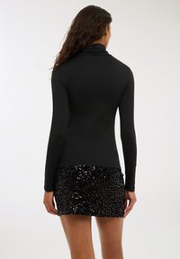 Top nero a maniche lunghe con colletto alto, design aderente, abbinato a una minigonna nera con paillettes lucide e sovrapposte.