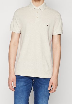 Beige polo med krave, to knapper og korte ærmer. Har en lille logo på venstre bryst. Bomuldsblanding med glat tekstur.