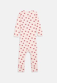Langarm rompertje van zacht roze stof met een herhalend patroon van kleine rode hartjes. Het heeft een ronde hals en een aansluitende pasvorm met voetjes.