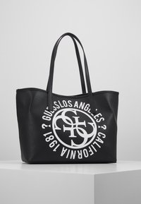 Czarna torba typu tote ze skóry z podwójnymi uchwytami, z okrągłą białą grafiką z tekstem. Gładka faktura i przemyślana konstrukcja.