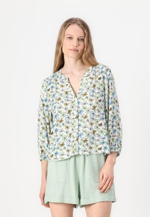 Bluse i lett materiale med blomsterpattern i hvitt, med grønne, blå og brune blomster, med V-hals og trekvart ermer. Kombinert med mintfargede shorts.