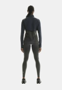 Veste de sport bleu marine et grise avec des manches longues, un col haut et une coupe ajustée, assortie à des leggings gris foncé et des chaussures noires texturées.