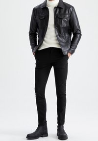 Veste en cuir noir avec deux poches avant, portée sur un col roulé texturé blanc, associée à un pantalon noir slim et des bottines.