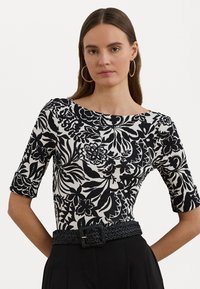 Top floreale in bianco e nero con maniche a tre quarti, scollatura a barca e finitura testurizzata, abbinato a una cintura nera intrecciata.