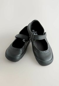 Czarne baleriny typu Mary Jane na rzepy z perforacjami w kształcie gwiazdek, rozmiar 12, ułożone skrzyżowane na jasnej powierzchni.