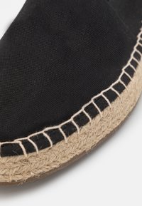Espadrille en toile noire avec une semelle en jute tressé, dotée d'une couture contrastante autour du bord pour plus de détails et de texture.
