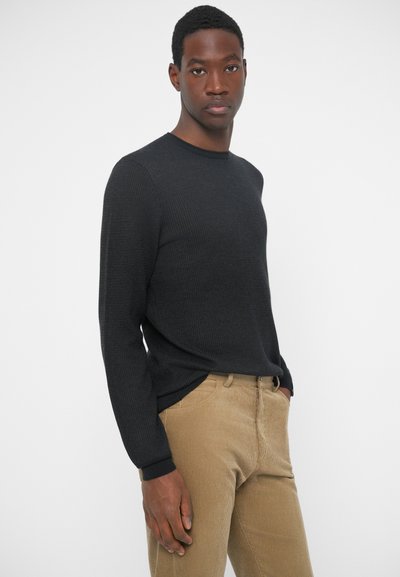 Sort ribbet langærmet sweater med rund hals, parret med beige kordfløjspants, der har sidelommer og en subtil tekstur.