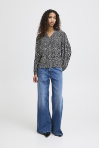 Blusa bianca e nera a fantasia con scollatura a V e maniche a palloncino, abbinata a jeans a vita alta blu svasati e scarpe nere con tacco.