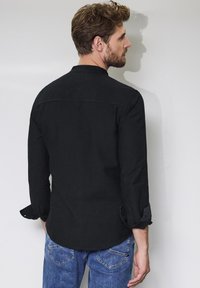 Camicetta nera a maniche lunghe con design a taglio dritto, polsi con bottoni e texture liscia, abbinata a jeans in denim blu.