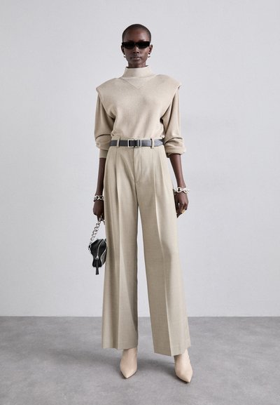 Beige tætsiddende sweater med skulderdetaljer, brede beige bukser, grå bælte, sort håndtaske med kæde og nude spidse hæle.