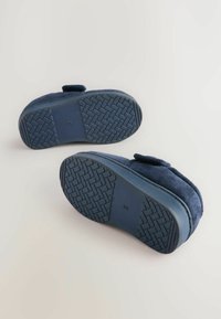 Pantofole blu navy con tomaia in morbido suede, suola in gomma resistente con un motivo di grip testurizzato e una fascia regolabile in Velcro.