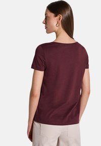 T-shirt bordeaux à manches courtes en coton, avec un col rond et une texture lisse. Présenté de dos.